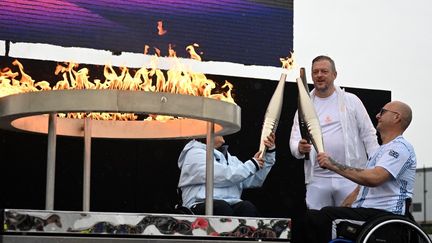 Helene Raynsford, championne de para-aviron et Gregor Ewan, médaillé de bronze en curling fauteuil allument la flamme paralympique au côté du président du Comité international paralympique Andrew Parsons, à Stoke Mandeville, le 24 août 2024. (JUSTIN TALLIS / AFP)