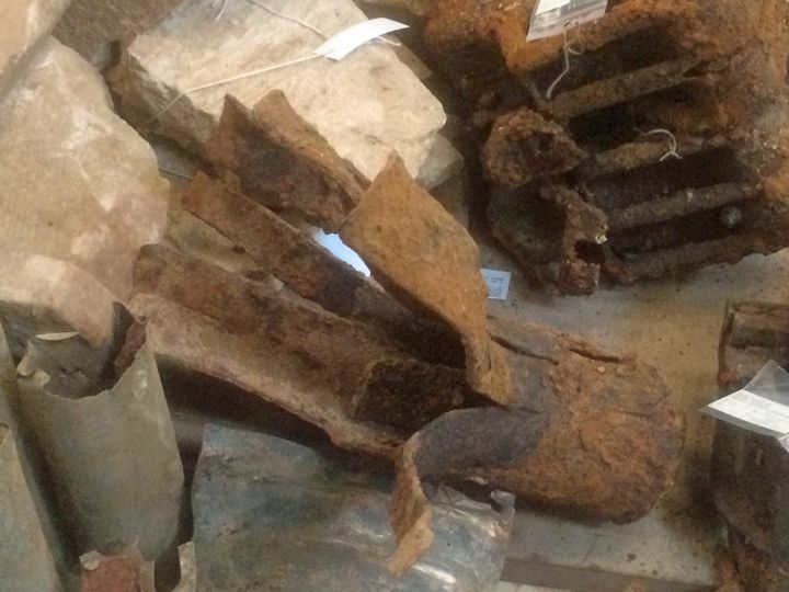 Objets divers découverts lors de fouilles sur des sites du débarquement de Normandie. Au milieu, un débris d'obus incendiaire allemand qui a explosé. ''Par leur côté rouillé, déchiqueté, ils renvoient à la violence des combats", constate un archéologue.
 (FTV - Laurent Ribadeau Dumas)