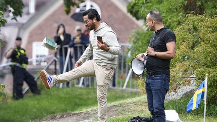 L'activiste irakien Salwan Momika donne un coup de pied dans un exemplaire du Coran à proximité de l'ambassade d'Irak à Stockholm, le 20 juillet 2023. (OSCAR OLSSON / TT NEWS AGENCY / AFP)