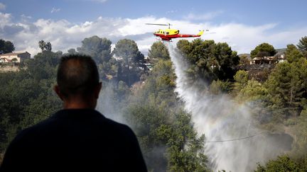 Un homme observe un hélicoptère tenter d'éteindre un incendie à Carros (Alpes-Maritimes), qui a ravagé 90 hectares, le 25 juillet 2017. (SEBASTIEN NOGIER / EPA)