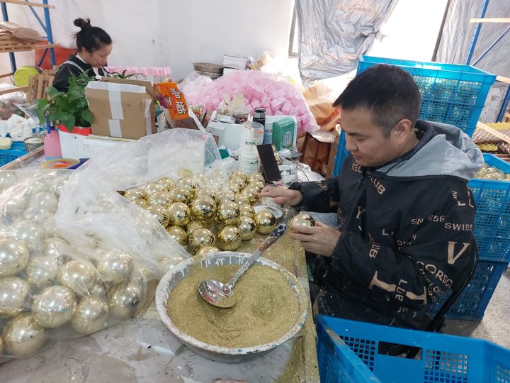 Ouvrier qui prépare une boule et qui colle dessus des paillettes dorées dans une usine de Yiwu, en Chine. (Sébastien Berriot / RADIO FRANCE)