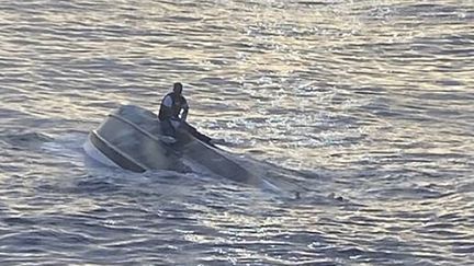 Un homme sur la coque d'un bateau près des côtes de la Floride, le 25 janvier 2022. (HANDOUT / US COAST GUARD / AFP)