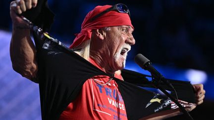 Le catcheur Hulk Hogan arrache un t-shirt pour révéler un débardeur "Trump-Vance", sur la scène, le 18 juillet 2024. "Que la Trumpmania jaillisse, mes frères !", s'écrie-t-il, qualifiant l'ancien président de "héros" et de "gladiateur", devant le principal intéressé, l'air ravi. (BRENDAN SMIALOWSKI / AFP)