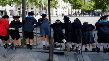 Sur les Champs-Elysées, des enfants attendent la venue d'Emmanuel Macron, où il doit défiler à bord d'un véhicule militaire. (CHARLY TRIBALLEAU / AFP)