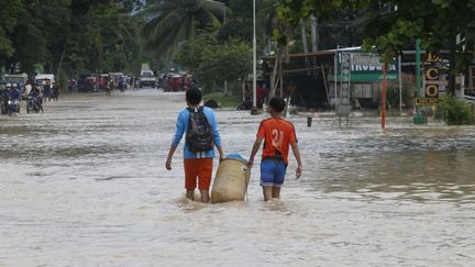 Des enfants transportent leurs affaires lors d'une inondation à Davao del Sur aux Philippines, en novembre 2022. (JEOFFREY MAITEM / AFP)