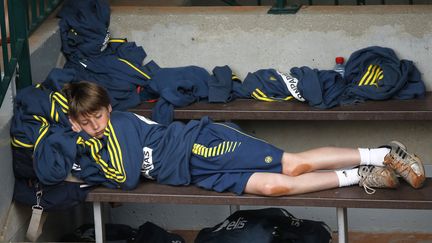 Un ramasseur de balles fait la sieste sur un banc, les genoux encore pleins de terre battue. (THOMAS COEX / AFP)