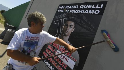 Un employé de Fiat collant une affiche pour protester contre le transfert de Cristiano Ronaldo à la Juventus Turin. On peut y lire : "Nous sommes ceux qui te payons". (FOTOGRAMMA / IPA / MAXPPP)