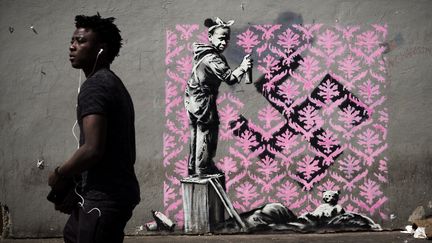 Un homme devant une œuvre attribuée au street artist Banksy, à Paris, le 24 juin 2018. (PHILIPPE LOPEZ / AFP)