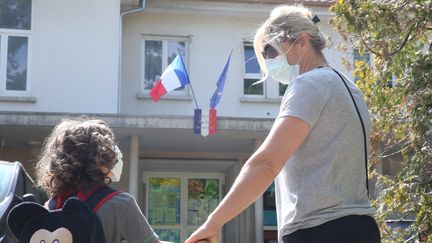 Un petit garçon et sa maman qui portent un masque devant une école. (photo d'illustration) (JEAN-FRANÇOIS FREY / MAXPPP)