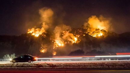 Aidé par des vents qui ont augmenté de manière spectaculaire, atteignant 130 km/h sur les hauteurs, les incendies continuaient de se propager au soir du 6 décembre 2017, comme ici l'incendie "Thomas", le long d'une route à Casitas Springs, au nord-ouest de Los Angeles. (KYLE GRILLOT / AFP)