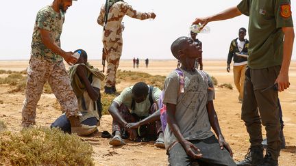 Les forces de sécurité libyennes donnent de l'eau à des migrants non loin de la localité d'Al 'Assah, le 30 juillet 2023. Sous une chaleur accablante, ces hommes racontent avoir été abandonnés à la frontière, en plein désert, par les autorités tunisiennes. (MAHMUD TURKIA / AFP)