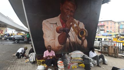 Sous le pont d'Ojuelegba, des marchands ambulants sont assis sous le portait du célèbre trompettiste nigérian Victor Abimbola Olaiya, connu sous le nom de Dr Victor Olaiya. Le musicien a connu son heure de gloire dans les années 1950 et 1960. (PIUS UTOMI EKPEI / AFP)