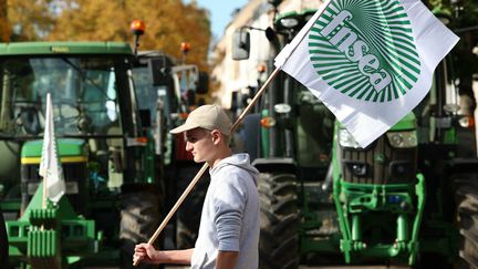 Un homme passe entre des tracteurs avec un drapeau de la FNSEA, lors d'une mobilisation d'agriculteurs le 21 octobre 2024 à Strasbourg (Bas-Rhin). (FREDERICK FLORIN / AFP)