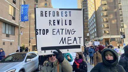 Un manifestant brandit une pancarte portant l'inscription "Reforester, réensauvager, arrêter de manger de la viande", lors la marche pour la nature, le 10 décembre 2022 à Montréal (Canada). (THOMAS BAIETTO / FRANCEINFO)