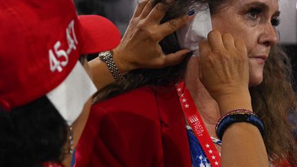 A la convention républicaine à Milwaukee, une déléguée de l'Arizona, Stacey Goodman (à gauche), place un bandage sur l'oreille d'une des membres du comité du Parti républicain, Liz Harris, le 17 juillet 2024. Depuis que Donald Trump a échappé à une tentative d'assassinat, l'accessoire témoigne du soutien au candidat conservateur. (JIM WATSON / AFP)