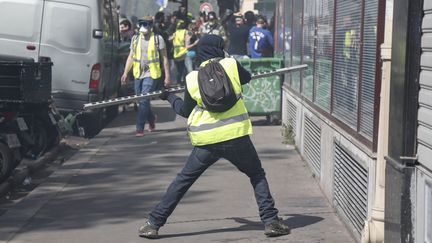 Un individu tente de briser une vitre, lors d'une manifestation de "gilets jaunes", à Paris le 20 avril 2019. (ZAKARIA ABDELKAFI / AFP)