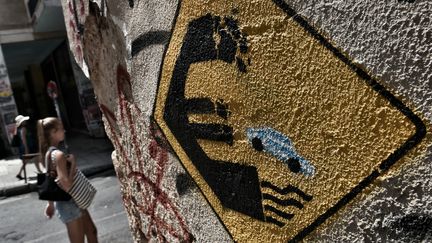 Une voiture chute d'un sigle euro, repr&eacute;sent&eacute; &agrave; la mani&egrave;re d'un panneau de signalisation sur un mur de la capitale grecque, le 28 juin 2015. (ARIS MESSINIS / AFP)