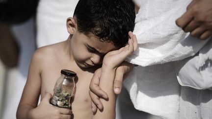 Un petit gar&ccedil;on tient une bouteille de cailloux &agrave; jeter contre des piliers pendant le rituel "Jamarat" de "lapidation de Satan". (MOHAMMED AL-SHAIKH / AFP)