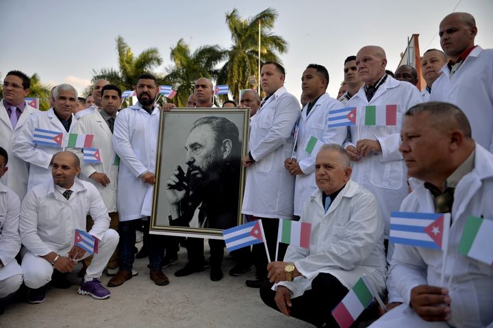 Les médecins et les infirmières de la Brigade médicale internationale Henry Reeve de Cuba posent avec un portrait de l'ancien président cubain Fidel Castro, alors qu'ils font leurs adieux, avant de se rendre en Italie durement touchée par la pandémie de coronavirus. Le 21 avril 2020.&nbsp; (YAMIL LAGE / AFP)