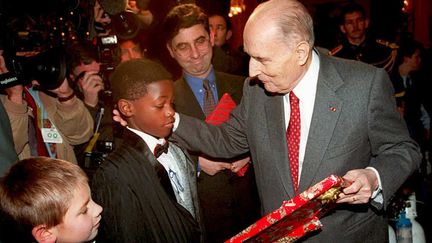 Quatorzi&egrave;me et dernier No&euml;l de Fran&ccedil;ois Mitterrand &agrave; l'Elys&eacute;e, le 21 d&eacute;cembre 1994. Le pr&eacute;sident se voit offrir un cadeau par un enfant. "C'est un portrait [de Fran&ccedil;ois Mitterrand]&nbsp;que mes parents ont ramen&eacute; du Za&iuml;re", expliquera le gar&ccedil;on aux cam&eacute;ras de France 2. (GERARD FOUET / AFP)