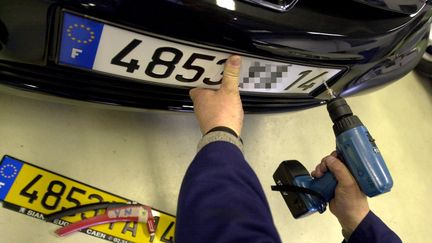 Un technicien installe une plaque d'immatriculation sur une voiture &agrave; Caen (Calvados), le 18 avril 2003. (MYCHELE DANIAU / AFP)