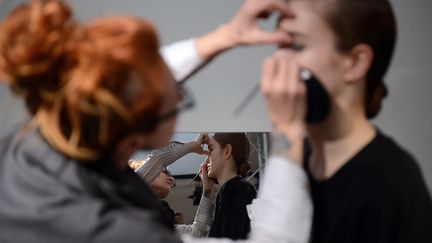 Une maquilleuse travaille sur le visage d'une jeune femme. (MARTIN BUREAU / AFP)