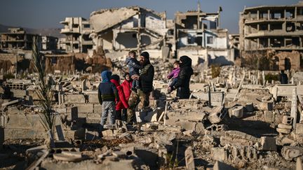 Une famille se tient devant des tombes détruites, dans un cimetière de Jobar (Syrie), le 18 décembre 2024. (ARIS MESSINIS / AFP)