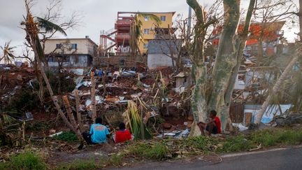 Des gens assis le 18 décembre auprès de ce qui reste de leur maison à Mamoudzou, après le passage du cyclone Chido à Mayotte. (DIMITAR DILKOFF / AFP)