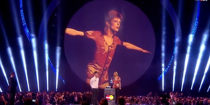 David Bowie plane sur les Brit Awards 2014, mais c'est Kate Moss qui vient recevoir son prix du Meilleur chanteur des mains de Noel Gallagher.
 (Brit Awards)