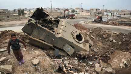 Dans un quartier est de Mossoul, le 21 janvier 2017, un enfant se tient près d'un véhicule détruit par les affrontements entre les forces irakiennes et Daesh (AHMAD AL-RUBAYE / AFP)