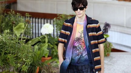 "Pourquoi avoir écrit en gros +YEAH!+ sur un T-shirt?" interroge un journaliste. "Pourquoi pas?" lui répond Sir Paul Smith. Le créateur injecte une bonne dose d'optimisme avec sa nouvelle collection, à coup de rayures couleur arc-en-ciel. "Please, relax. Will you please relax!" lâche-t-il encore, afin d'expliquer l'esprit de ses créations. Des plantes en pot ont été posées sous la coupole de la Bourse du Commerce. On les retrouve ici et là, colorées, sur les vêtements. Les mannequins n'ont pas l'air stressé, en effet. Leurs pantalons et bermudas larges semblent ultra-confortables. La chemisette est ouverte sur un T-shirt coloré, le jogging peut se porter avec une veste. Même en costume, également larges, ils ont l'air cool. Des coccinelles, des bananes, des cannettes avec paille sont représentées sur les habits. Plus sérieux: des chevrons, très années 70, décorent hauts et pantalons. Les tissus se juxtaposent, comme dans une veste qui joue sur le mat et le brillant. Paul Smith a beaucoup utilisé de satin dans cette collection, qui mixe une mode ludique et colorée à des tons plus sombres, du gris au bleu pétrole.
 (PATRICK KOVARIK / AFP)