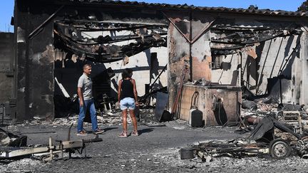 Un couple inspecte les dégâts autour d'une maison brûlée par les flammes à Bormes-les-Mimosas (Var), le 26 juillet 2017. (ANNE-CHRISTINE POUJOULAT / AFP)