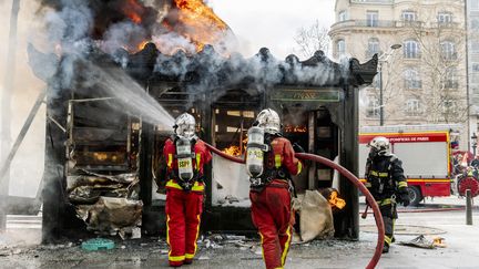 Des pompiers éteignent un kiosque en flammes sur les Champs-Elysées, à Paris, le 16 mars 2019. (JONATHAN PHILIPPE LEVY / HANS LUCAS / AFP)