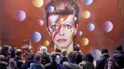 La foule se rassemble pour rendre hommage à David Bowie sous une fresque à l'effigie du chanteur, le 11 janvier 2016 à Brixton, au sud de Londres (Royaume-Uni). L'icône de la musique britannique est morte des suites d'un cancer, la veille, à l'âge de 69 ans. (NIKLAS HALLE'N / AFP)