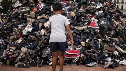 Un enfant dépose une paire de chaussures sur la pyramide syndicale d'Handicap International, pour dénoncer les mines antipersonnels, en 2014 à Lyon (Rhône). (JEFF PACHOUD / AFP)