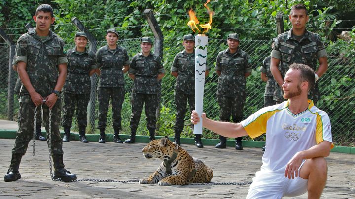 Un athlète tient la flamme olympique devant 