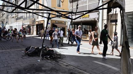 Des piétons passent devant une tonnelle de magasin brûlée dans le centre de Marseille, , le 1er juillet 2023. (CLEMENT MAHOUDEAU / AFP)