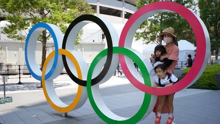 Des Japonais posent derrière l'emblème des JO&nbsp;à côté du stade&nbsp;olympique&nbsp;à Tokyo, le 20 juillet 2021. (NAOKI MAEDA / YOMIURI / AFP)