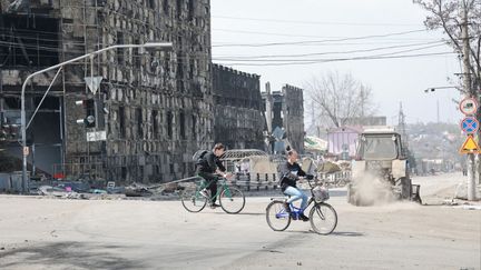 Des habitants font du vélo à Marioupol, en Ukraine, le 18 avril 2022. (SERGEY AVERIN / SPUTNIK / AFP)