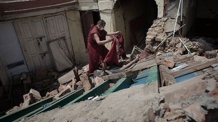 dont la famille vit sur le site de Swayambunath depuis des siècles, s’est installé avec 200 autres personnes dans un campement de fortune, en bordure du monument, pour surveiller le temple des singes. La nuit, «on ne dort pas. On surveille. Je veux empêcher les pillages de statues», explique-t-il à la journaliste Beatrice Le Bohec. Ici sur la photo, un moine essaye de récupérer médicaments, ustensiles de cuisine et quelques habits.   ( AFP PHOTO / Nicolas ASFOURI)