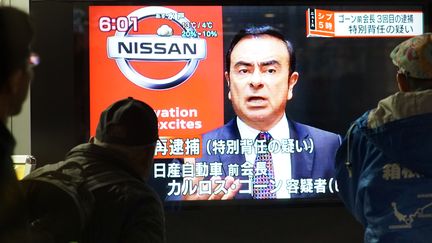 Des passants regardent un écran de télévision où apparaît Carlos Ghosn, à Tokyo (Japon), le 21 décembre 2018. (KAZUHIRO NOGI / AFP)