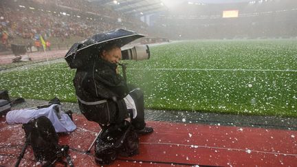 Un photographe se prot&egrave;ge lors d'une averse de gr&ecirc;le pendant le match amical de football opposant la Belgique &agrave; la Tunisie &agrave; Bruxelles (Belgique), le 7 juin 2014. (MAXPPP)