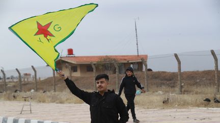 Un jeune homme brandit le drapeau du YPG, le groupement des unités de protection du peuple kurde, près de Qamishli en Syrie, le 8 décembre 2024. (DELIL SOULEIMAN / AFP)