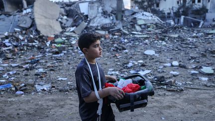 Un jeune Palestinien transporte des objets récupérés après une frappe israélienne sur la bande de Gaza, le 16 octobre 2023. (MOHAMMED ABED / AFP)