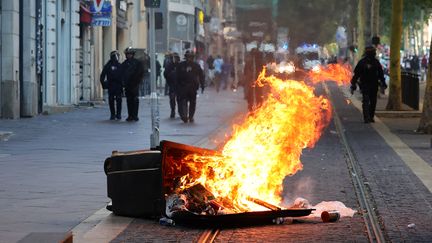 Des policiers devant une poubelle brûlée lors d'une manifestation après la mort de Nahel, le 1er juillet 2023, à Marseille (Bouches-du-Rhône). (CLEMENT MAHOUDEAU / AFP)