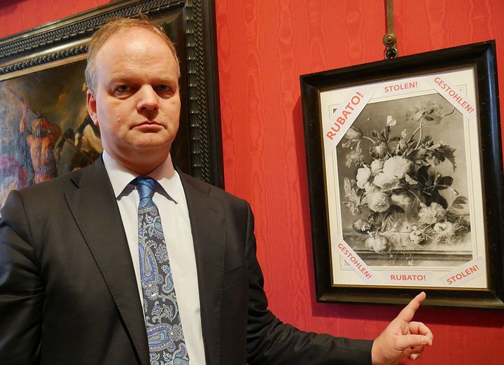 Eike Schmidt pose devant une copie en noir et blanc du tableau "Vaso di fiori" (Pot de fleurs) du peintre hollondais Jan van Huysum avec la mention "volé" en trois langues. (AFP / FLORENCE MUSEUM PRESS OFFICE)