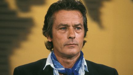 A "Paris-Match", en 2018, à la question de savoir si vieillir était une souffrance pour lui, Alain Delon répondait : "L'âge a ses conséquences. J'ai du mal à marcher, je dors beaucoup et je deviens gourmand ! Mais quand je vois les affiches dans Paris avec des photos de moi dans 'La Piscine' [il faisait sans doute référence à la campagne d'un célèbre parfum de couturier], je me dis qu'ils n'ont toujours pas trouvé mieux depuis." (Alain Delon sur le plateau d'une émission télévisée, 26 août 1985, Paris. PATRICK AVENTURIER  / GAMMA-RAPHO / GETTY IMAGES)