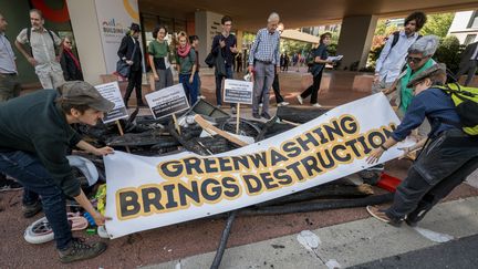 Des militants dénonçant l'écoblanchiment déploient une banderole à Genève (Suisse), le 3 octobre 2023. (FABRICE COFFRINI / AFP)