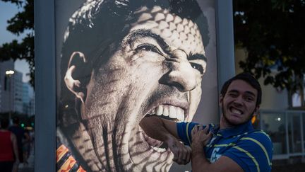 Un touriste prend la pose devant une publicit&eacute; sur laquelle appara&icirc;t le joueur uruguyen Luis Suarez, suspendu apr&egrave;s avoir mordu un joueur durant la Coupe du monde de football &agrave; Rio de Janeiro (Br&eacute;sil), le 26 juin 2014. (YASUYOSHI CHIBA / AFP)