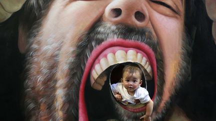 Un b&eacute;b&eacute; pose dans une peinture en 3D lors d'une exposition d'art &agrave; Changsha (Chine), le 13 octobre 2013. (LI GA / XINHUA / AFP)